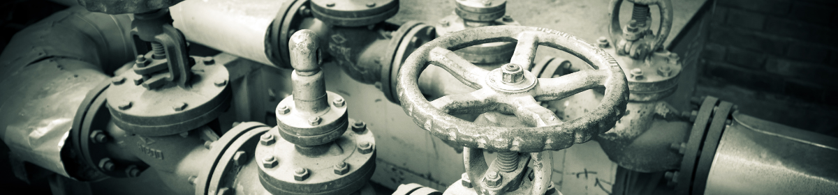 Close-up view of industrial metal control valves and piping system, showing aged and weathered valve wheels used for regulating fluid flow.