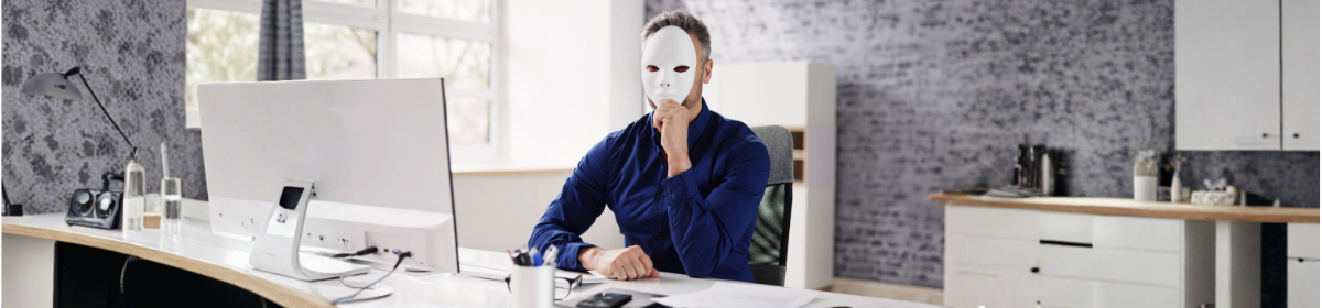 Man wearing a white mask sitting at a desk in front of a computer