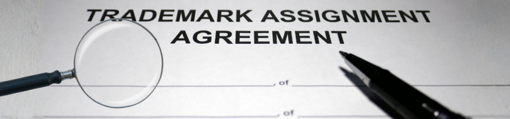 A magnifying glass and a pen placed over a document titled Trademark Assignment Agreement.