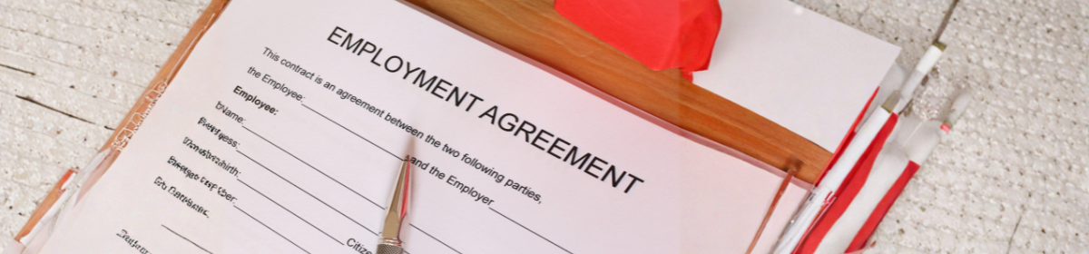 Close-up of an employment agreement document on a clipboard with a pen placed on top, surrounded by office supplies on a textured surface.