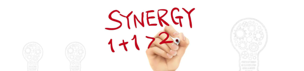 A hand writing the word “SYNERGY” above the equation “1 + 1 > 2” in red marker, illustrating the concept that combined elements can produce a greater effect than their individual contributions.