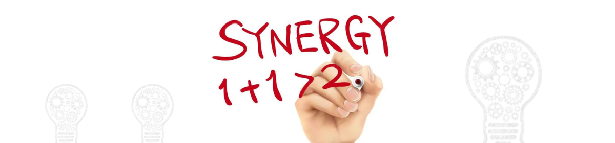 A hand writing the word “SYNERGY” above the equation “1 + 1 > 2” in red marker, illustrating the concept that combined elements can produce a greater effect than their individual contributions.