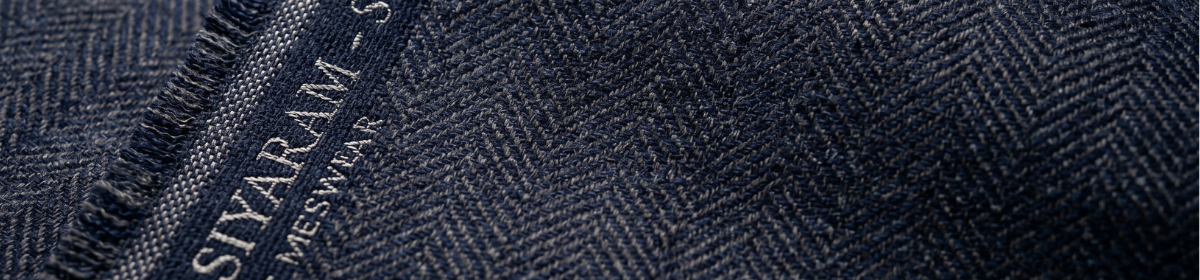 Close-up macro photograph of premium suiting fabric in deep navy and charcoal grey, with a fine herringbone or pinstripe weave pattern. Along the selvedge edge, the word "Siyaram" appears subtly woven or embossed into the cloth in a slightly lighter thread.