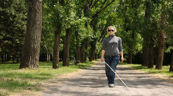 This image depicts a blind woman holding a stick and walking on a road. This image is relevant as a patent has been awarded for vibrating clothes which will help the blind person to navigate easily. Click on this image for more information